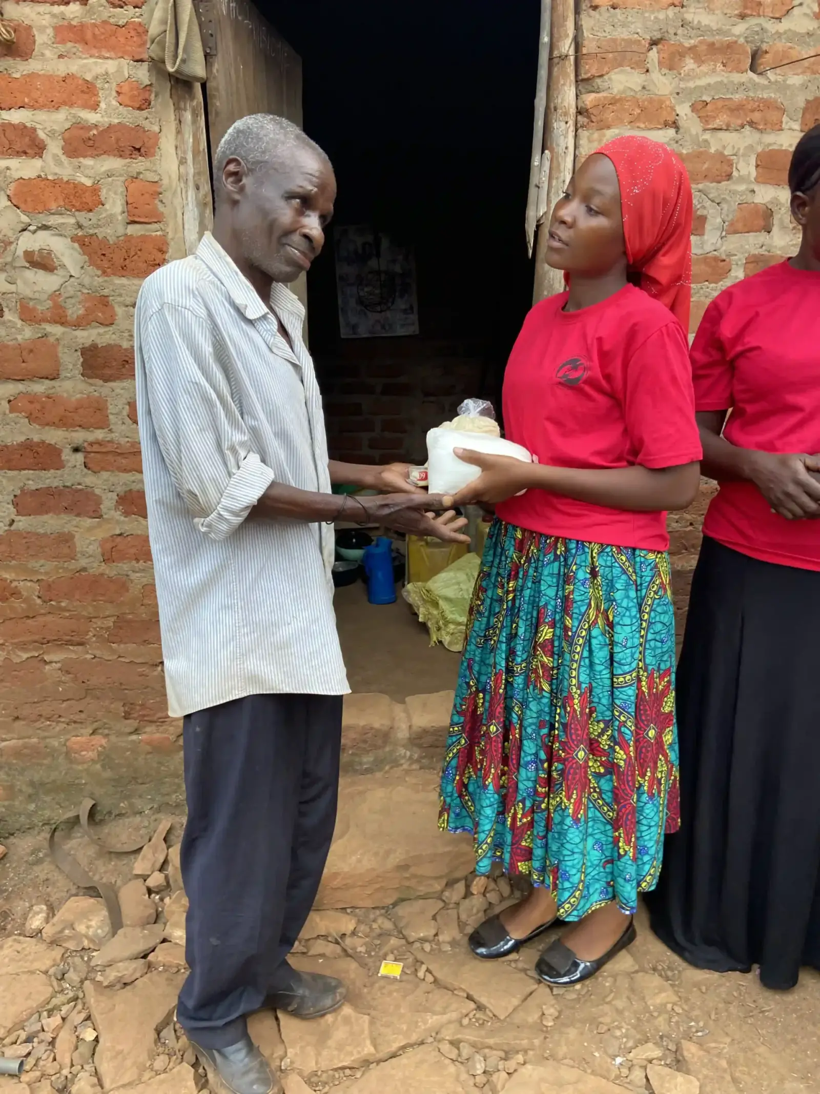 A volunteer handing a bag of food to an elderly man outside his home