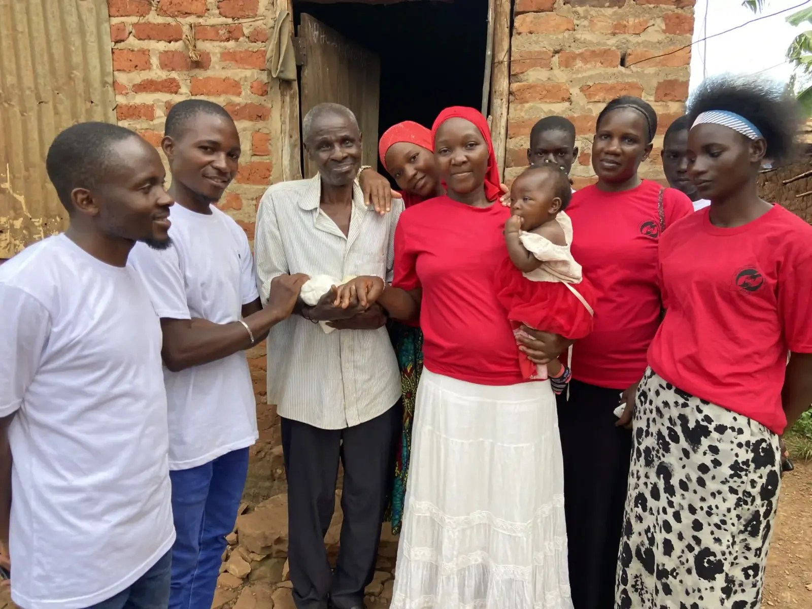 The team handing a gift to an elderly man, with a mother and baby beside them